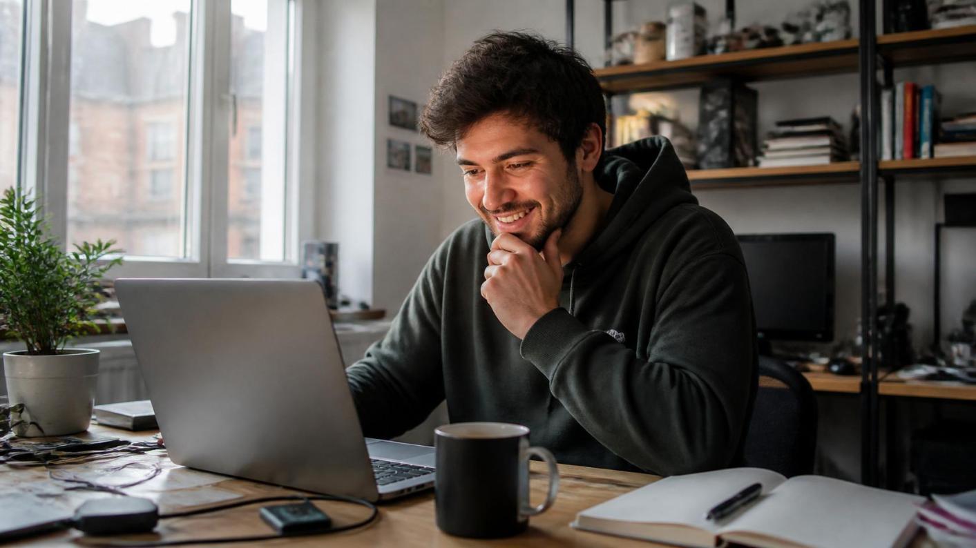 A developer smiles at his laptop, thrilled by his growing online software community.